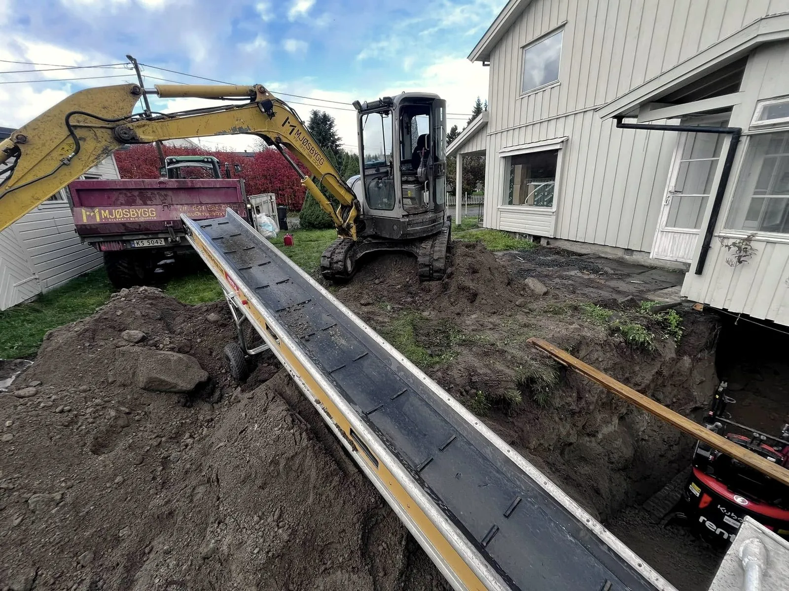 Gravemaskin og transportbånd ved huset
